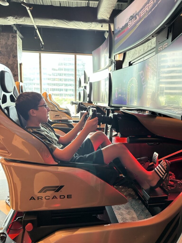 Ashley Wali's son enjoys playing on a racing game at F1 Arcade in Boston, Massachusetts.