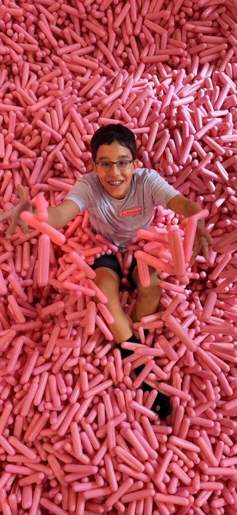 Ashley Wali's son smiles as he sits in the Sprinkle Pit of giant sprinkles at the Museum of Ice Cream in Boston, Massachusetts.